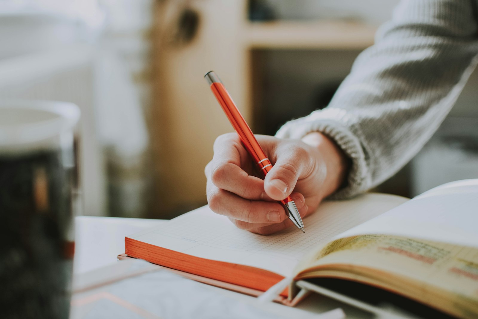 Manos escribiendo en un cuaderno abierto junto a una taza