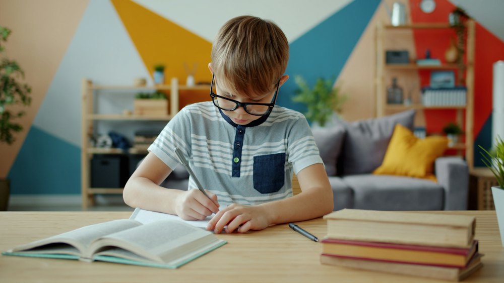 Niño con gafas escribiendo en un cuaderno en casa